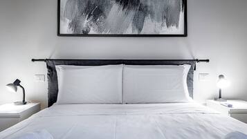 A modern hotel room with a large bed, two bedside tables, and a black abstract painting on the wall.