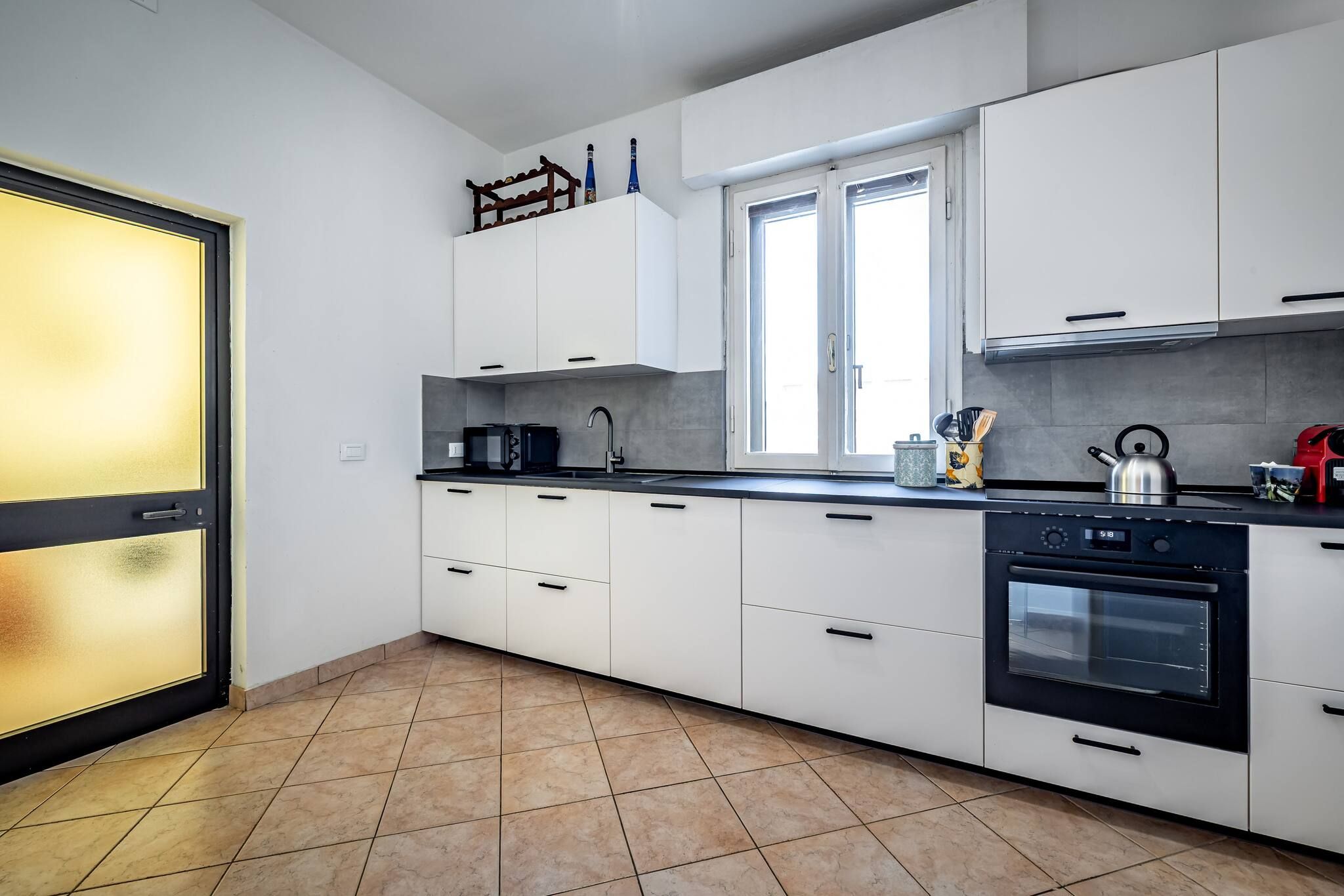 Une cuisine moderne avec des meubles blancs, une cuisinière noire et une fenêtre équipée de stores.
