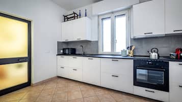 Une cuisine moderne avec des meubles blancs, une cuisinière noire et une fenêtre équipée de stores.