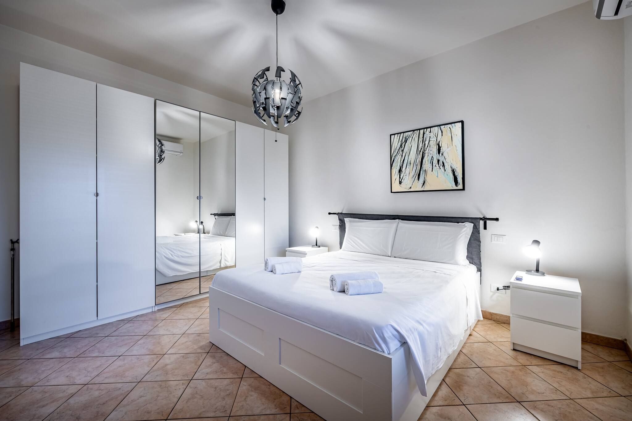 Un dormitorio moderno con una cama grande, una mesita de noche con lámpara, un armario y una lámpara en el techo.