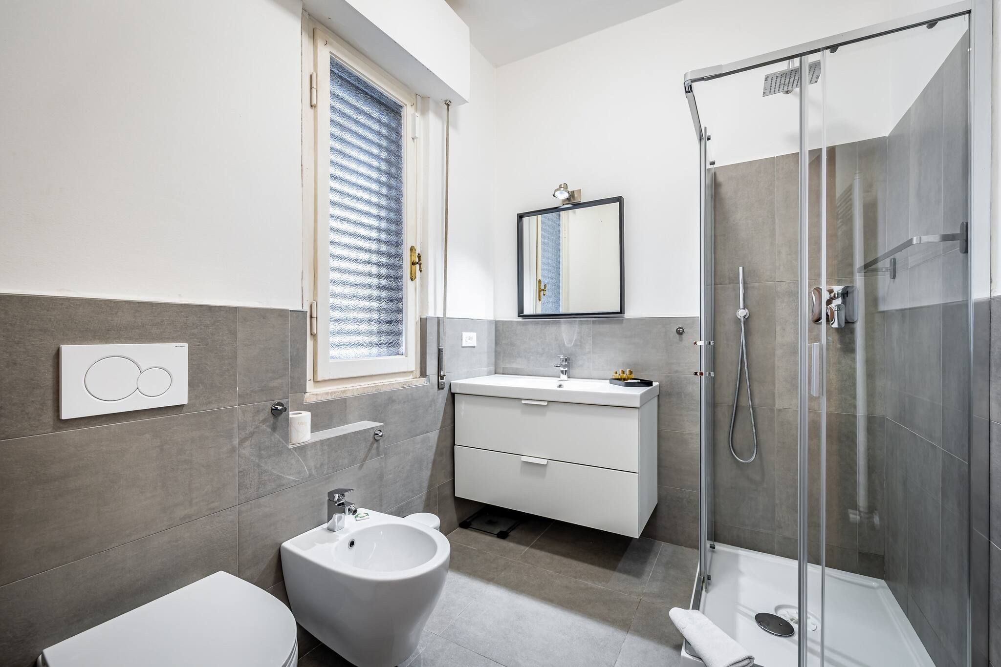Un baño moderno con bidé, inodoro y ducha con mampara de vidrio.