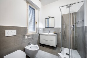 Un baño moderno con bidé, inodoro y ducha con mampara de vidrio.