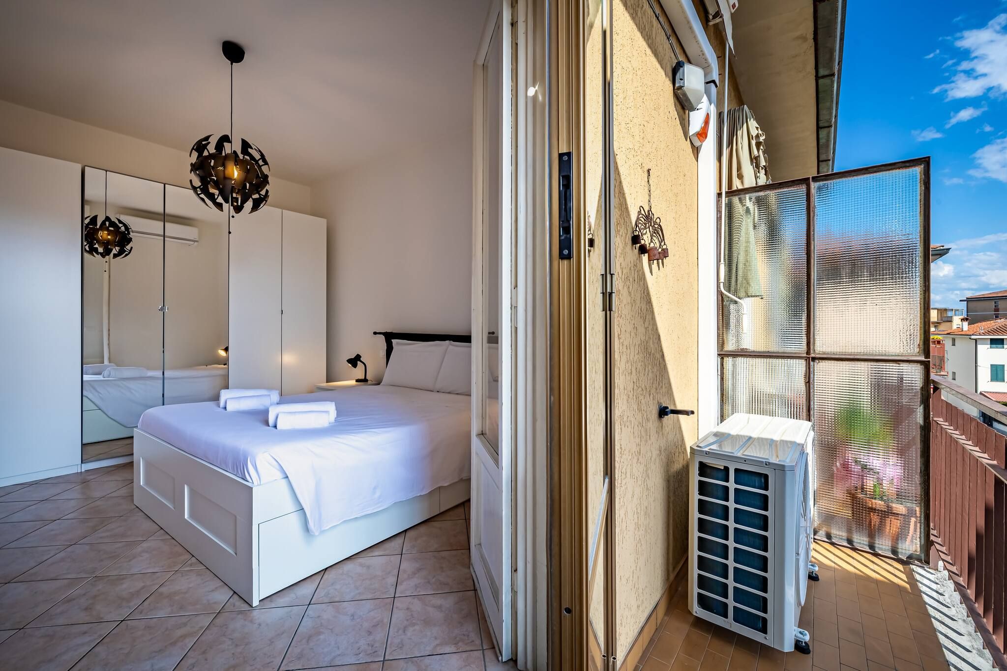 Un dormitorio con cama, un espejo grande, un armario y una puerta corrediza de vidrio que da a un balcón.