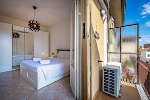 Un dormitorio con cama, un espejo grande, un armario y una puerta corrediza de vidrio que da a un balcón.