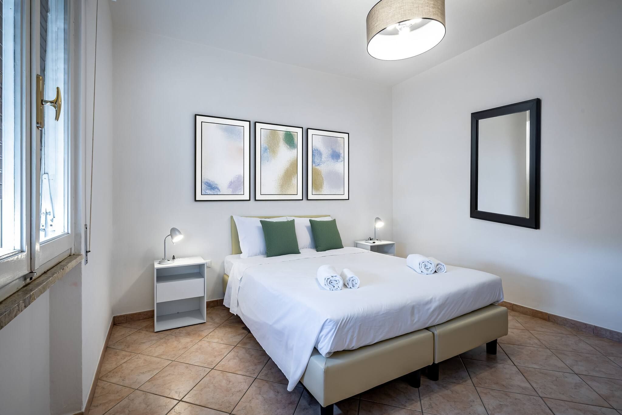 A clean, modern hotel room with a large bed, two bedside tables, a nightstand, and a wall-mounted mirror.