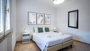 A clean, modern hotel room with a large bed, two bedside tables, a nightstand, and a wall-mounted mirror.