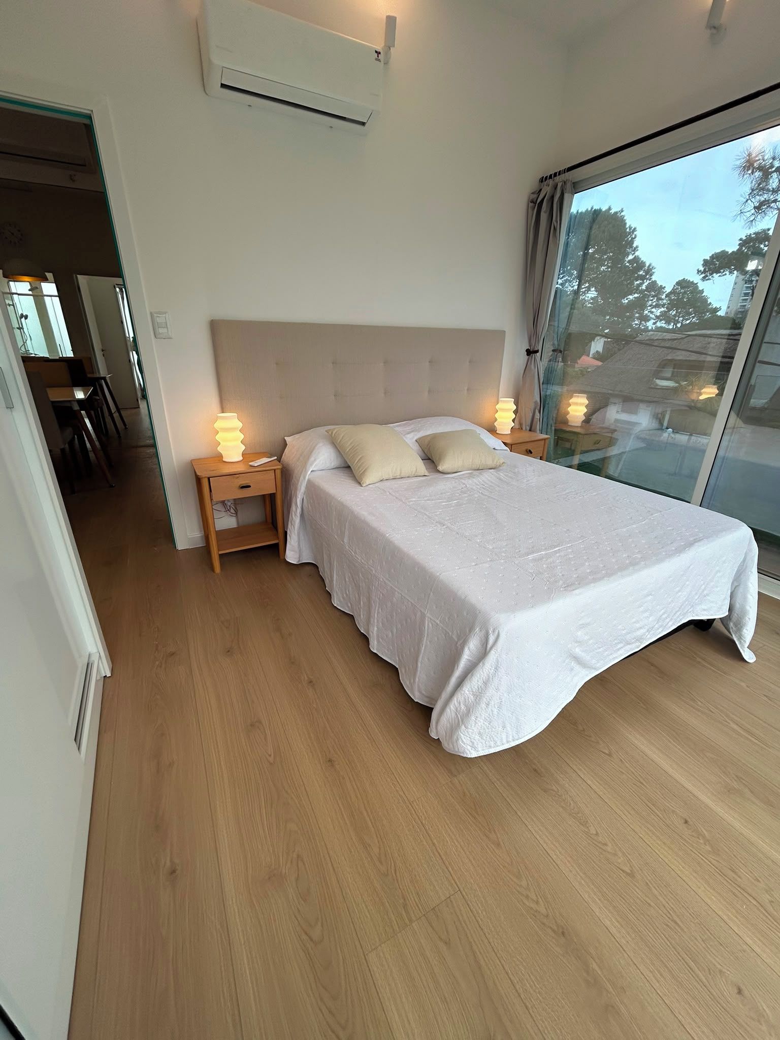 Un dormitorio con una cama, lámparas de noche y un ventanal amplio.