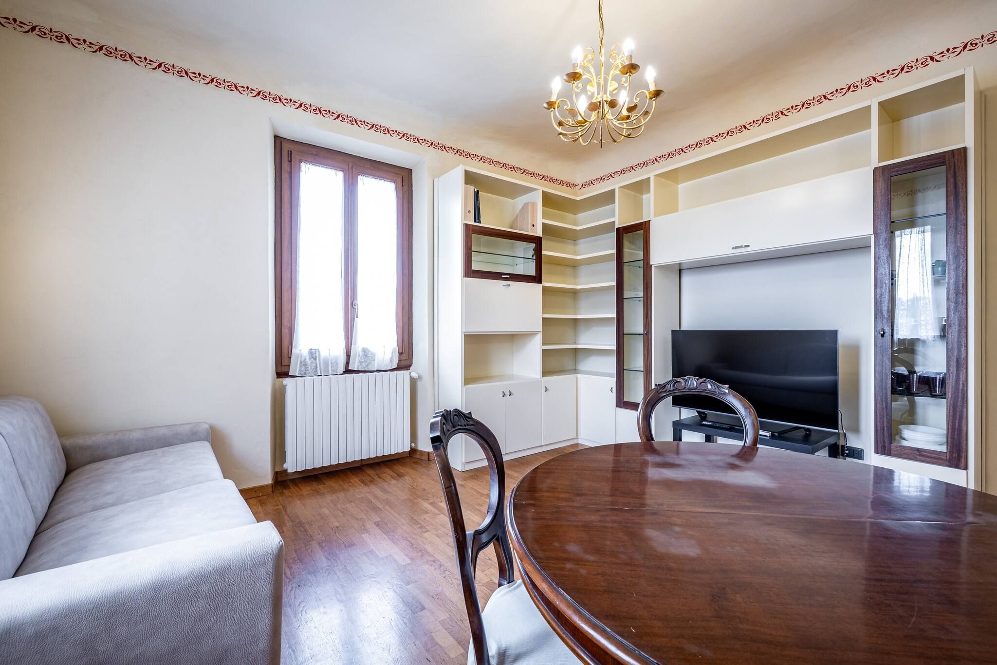 Un comedor con una mesa y sillas de madera, un sofá, un televisor y estanterías empotradas.