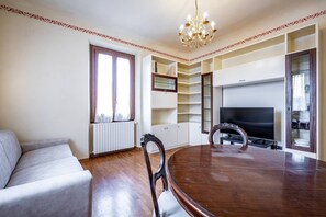 Uma área de refeições com mesa e cadeiras de madeira, um sofá, uma TV e estantes embutidas.