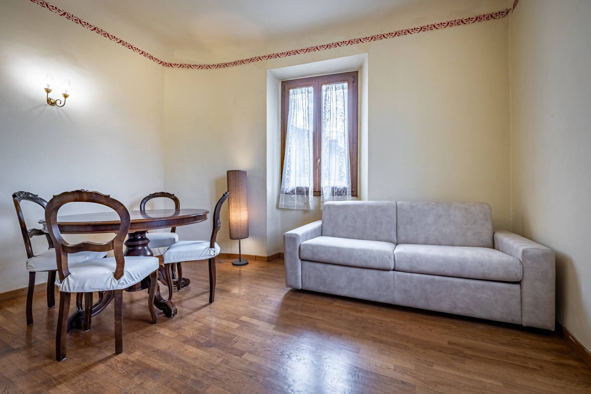 Una habitación con una mesa de comedor y sillas, un sofá, una lámpara y una ventana con cortinas.