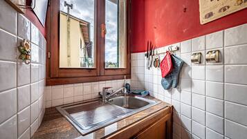 Una cocina con ventana, azulejos blancos, un lavamanos y una pared roja.