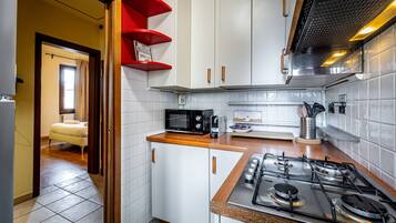 A kitchen with white cabinets, a gas stove, a microwave, and a red shelf.
