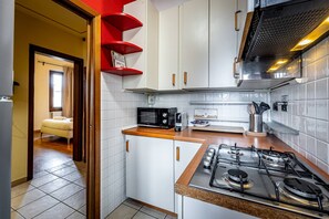 Uma cozinha com armários brancos, fogão a gás, micro-ondas e uma prateleira vermelha.