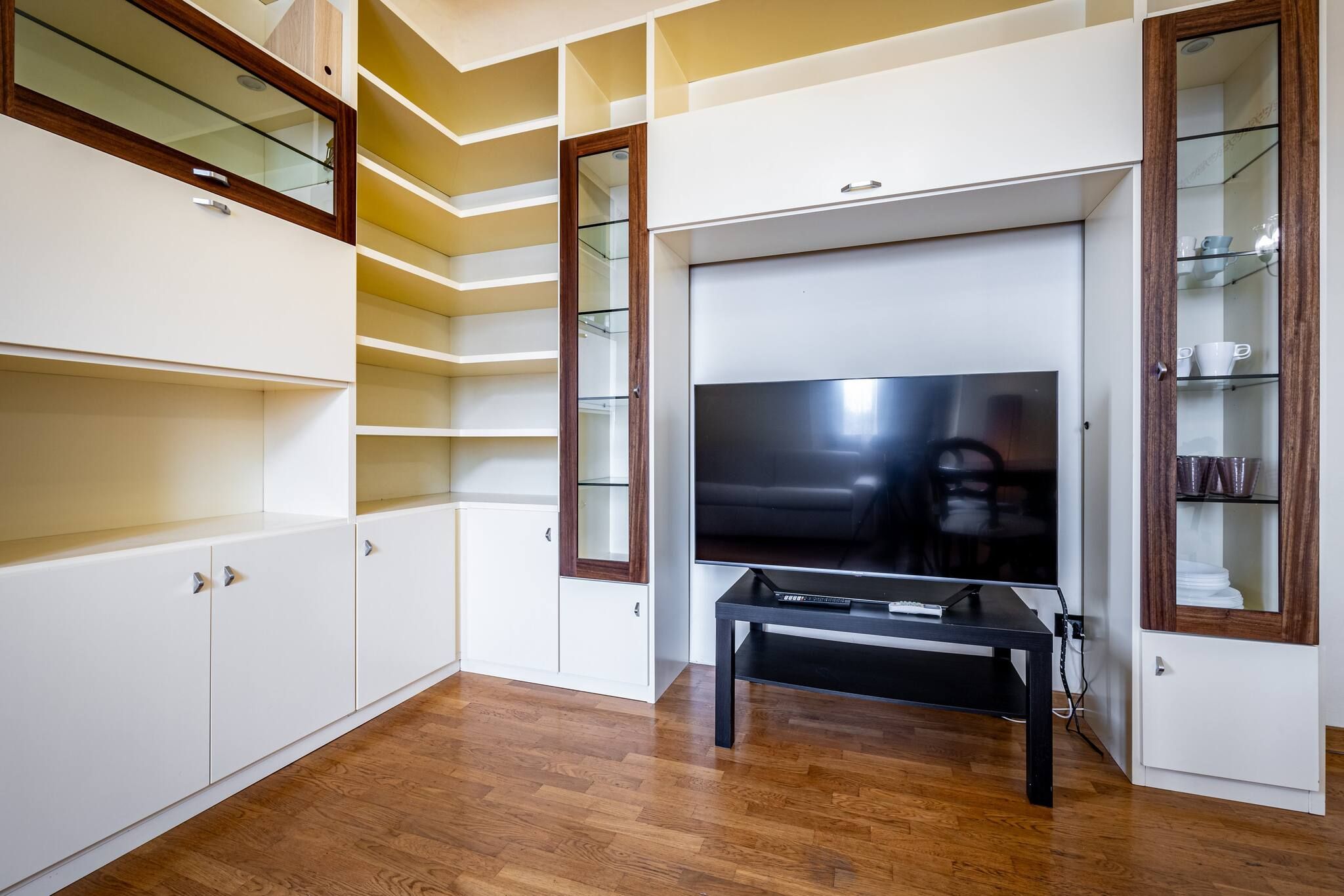 Un soggiorno moderno con televisore a schermo piatto, pavimento in legno, scaffalature integrate e una vetrina.