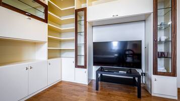 Un soggiorno moderno con televisore a schermo piatto, pavimento in legno, scaffalature integrate e una vetrina.