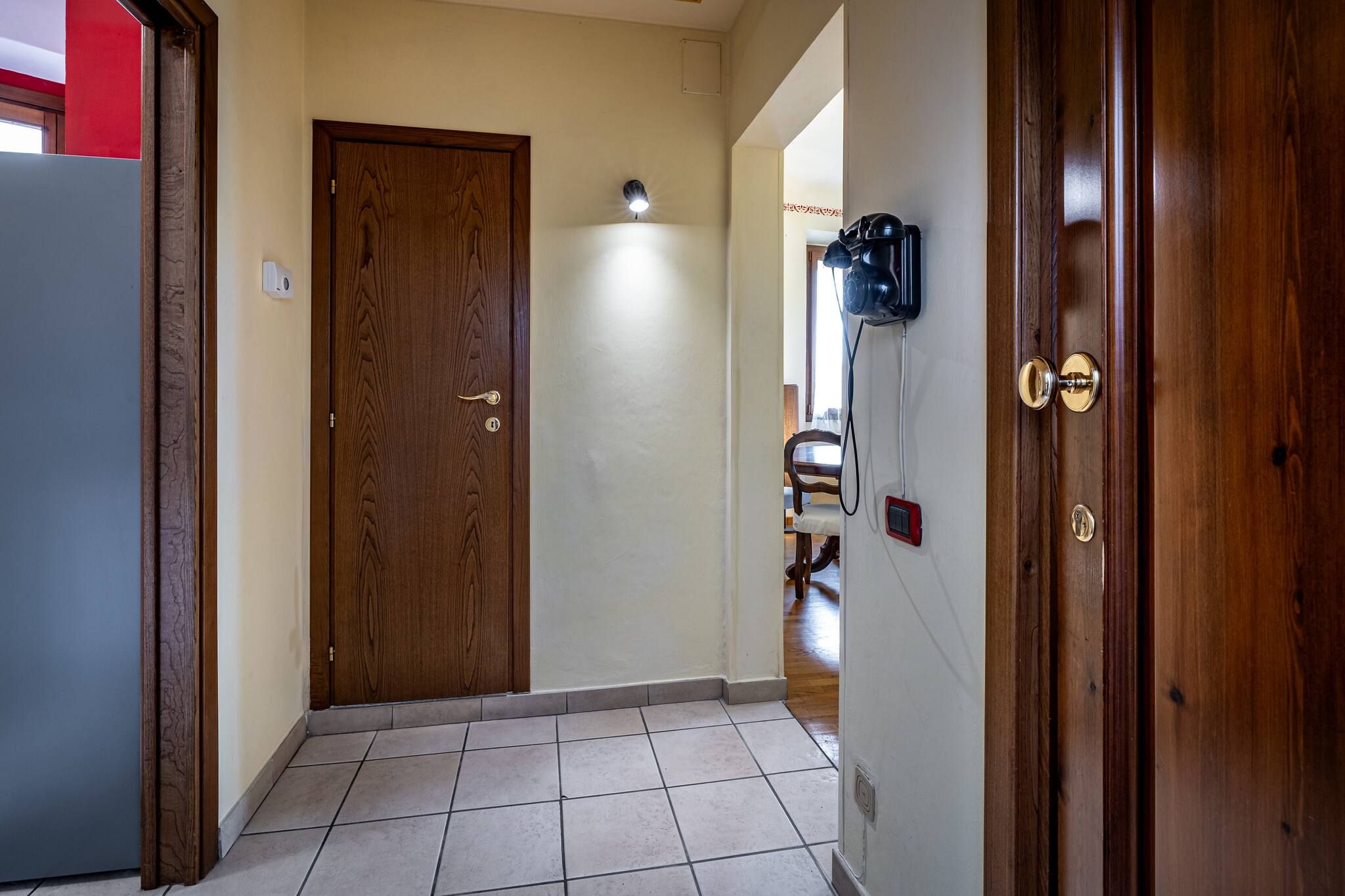 Un pasillo con una puerta de madera, una lámpara en la pared y un timbre.