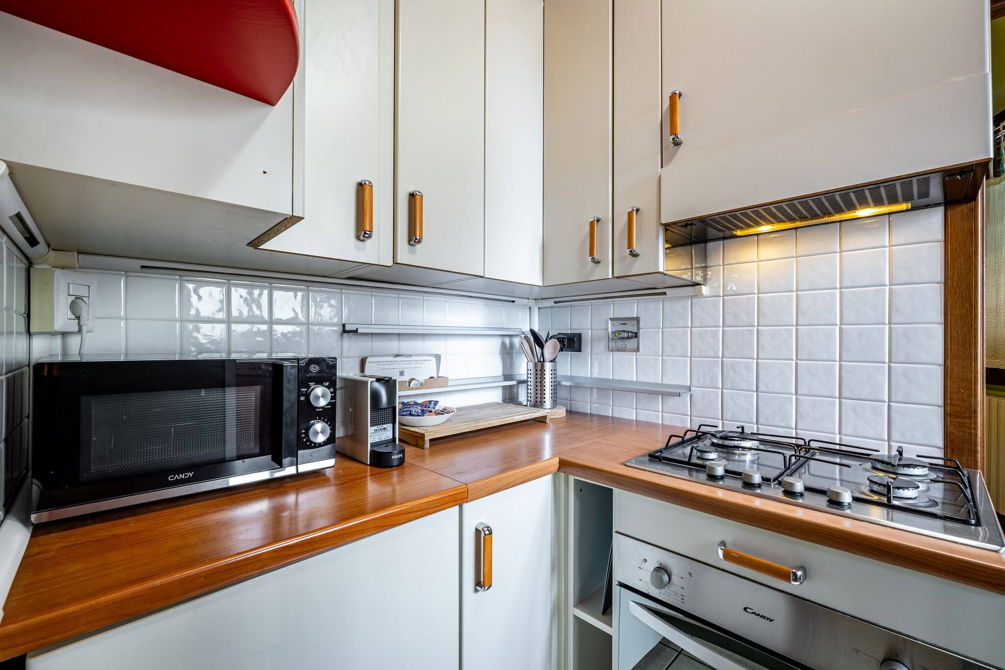 Uma cozinha compacta com armários brancos, micro-ondas, fogão a gás e forno pequeno.