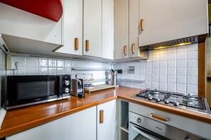 Une cuisine compacte avec des meubles blancs, un four à micro-ondes, une cuisinière à gaz et un petit four.