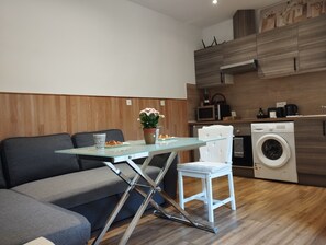Ein modernes Wohnzimmer mit Glastisch, einer Couch, einem Sessel und einem kleinen Tisch mit Topfpflanze.