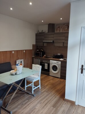 Cozinha compacta equipada com micro-ondas, forno e máquina de lavar roupa, mesa de jantar com cadeiras e um pequeno espaço de estar.