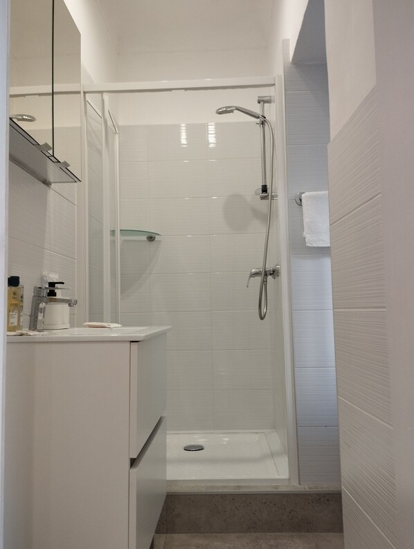 Casa de banho moderna com chuveiro envolto em vidro, lavatório branco e espelho em cima.