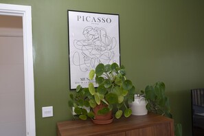 A framed artwork of Picasso's 'The Hug' on a green wall, with a wooden cabinet below holding potted plants. - The Greenwich Green | 2BR • 2BA • Balcony - Pass the Keys (London)