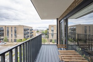A balcony with a view of modern buildings, a wooden bench, and a glass door. - The Greenwich Green | 2BR • 2BA • Balcony - Pass the Keys (London)
