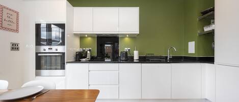 A modern kitchen with white cabinets, a black countertop, and a green accent wall.