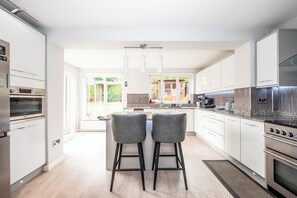 A modern kitchen with two bar stools, stainless steel appliances, and a view to the outdoors. - The Willow House | 4BR • Garden • Parking for 2 - Pass the Keys (Sidcup)