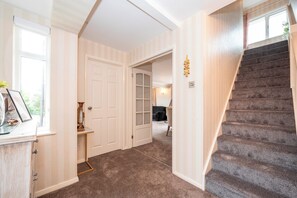 Un pasillo con piso alfombrado, una escalera y una puerta que da a otra habitación.