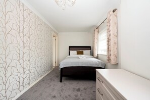 A bedroom with a bed, a dresser, a window with curtains, and a wall with a tree pattern. - The Willow House | 4BR • Garden • Parking for 2 - Pass the Keys (Sidcup)