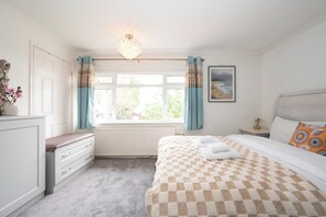 A bedroom with a bed, a dresser, a radiator, a window with curtains, and a painting on the wall. - The Willow House | 4BR • Garden • Parking for 2 - Pass the Keys (Sidcup)