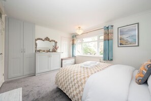 Un dormitorio con cama, cómoda, espejo, ventana con cortinas y un cuadro en la pared.