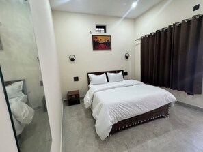 Ein Hotelzimmer mit Bett, Nachttisch, Wandleuchte, Fenster mit Vorhängen und einem Bild an der Wand.