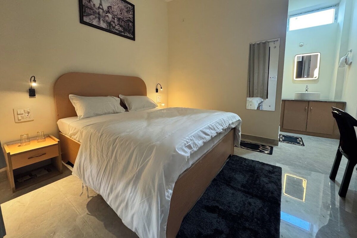 Ein Hotelzimmer mit Bett, Nachttischen, Teppich, Badezimmer mit Waschbecken und Spiegel sowie einem gerahmten Bild an der Wand.