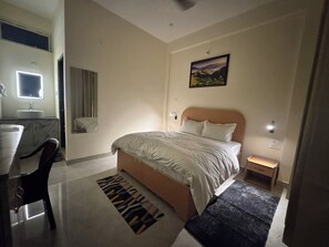A hotel room with a bed, bedside table, nightstand, and a desk with a chair. - Shivlok Residency (Barkot)