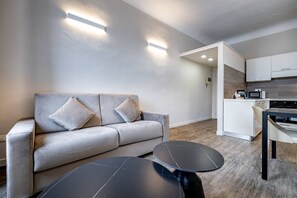 A modern living room with a grey sofa, two black round tables, and a kitchen area with white cabinets and a microwave. - Scala 111 3P (Florence)