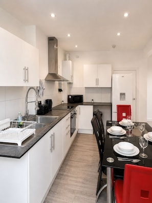 A modern kitchen with white cabinetry, a black countertop, and a dining area with a black table and red chairs. - Central 3BR | Brighton Station Walk to Beach (Brighton and Hove)