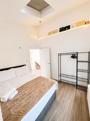 A hotel room with a bed, a skylight, a white door, a black metal shelf unit, and a wooden floor. - Central 3BR | Brighton Station Walk to Beach (Brighton and Hove)