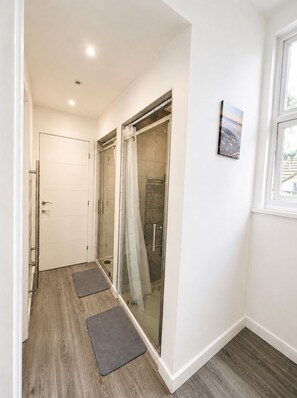 A hallway with a glass door leading to a shower area, a door on the left, and a window on the right. - Central 3BR | Brighton Station Walk to Beach (Brighton and Hove)