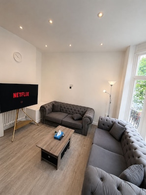 A modern living room with a flat-screen TV, two grey sofas, a wooden coffee table, and a floor lamp. - Central 3BR | Brighton Station Walk to Beach (Brighton and Hove)