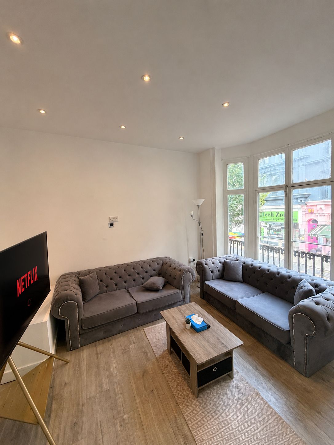 Een moderne woonkamer met twee grijze banken, een houten salontafel en een televisie waarop 'NETFLIX' staat.