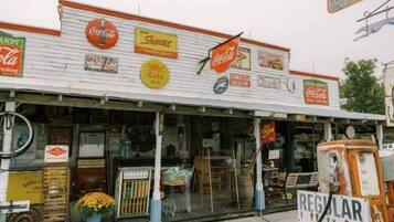 A vintage storefront with multiple Coca-Cola signs, a gas pump, and various vintage items displayed outside.