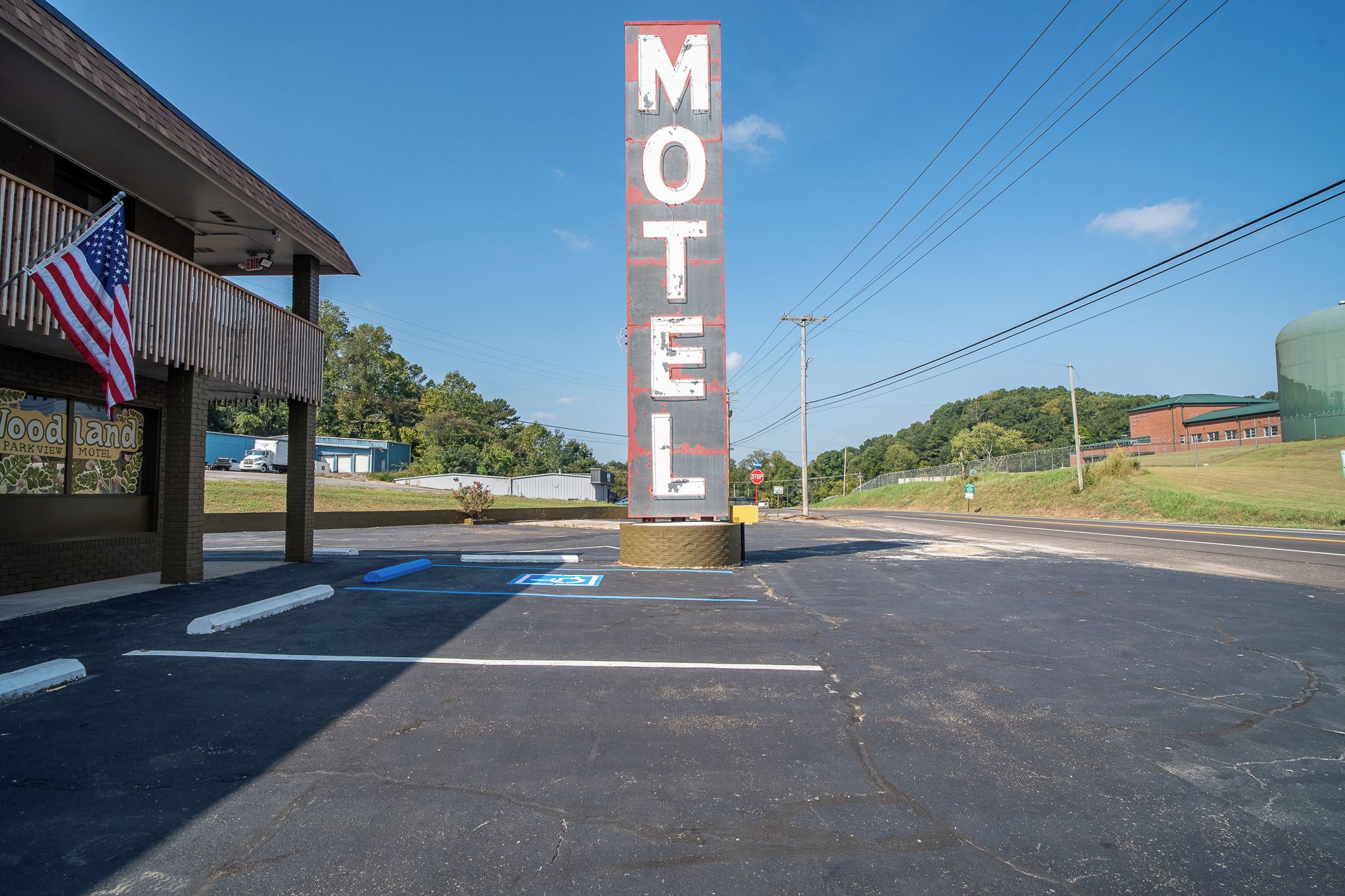Ein Motel mit einer auffälligen vertikalen Schautafel, einem Parkplatz mit eingezeichneten Stellplätzen und einem Gebäude, dessen Schild 'Woodland Parkview Motel' zeigt.