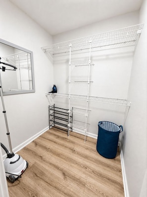 A storage closet with metal shelving units, a vacuum cleaner, and a blue laundry basket. - Across from Shands | 2BR Condo Near UF + Pool (Gainesville)