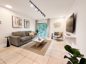 A modern living room with a sofa, coffee table, and a TV mounted on the wall. - Across from Shands | 2BR Condo Near UF + Pool (Gainesville)
