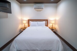 Habitación de hotel con cama, dos lámparas de noche, un equipo de aire acondicionado y cabecero de madera.
