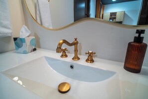 Un baño con un lavamanos blanco, dos grifos dorados, una caja de pañuelos y una botella de jabón.
