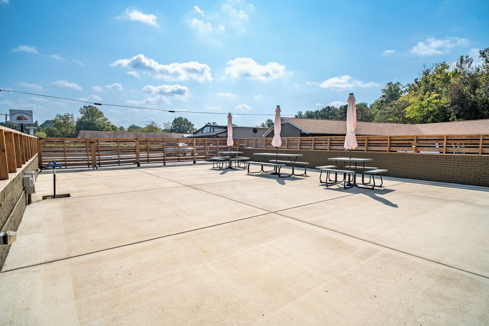 Un espace extérieur aménagé en terrasse, avec des tables de pique-nique et des parasols, entouré d’une clôture en bois et d’un mur de briques.