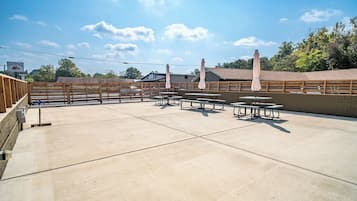 An outdoor patio area with picnic tables and umbrellas, surrounded by wooden fencing and a brick wall.